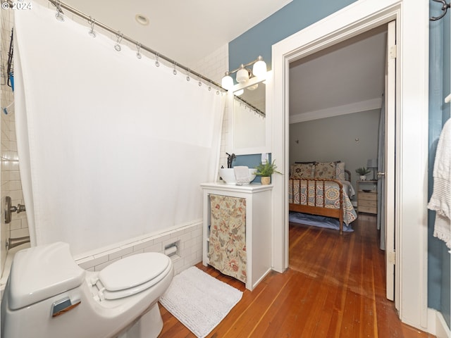 bathroom with hardwood / wood-style floors, toilet, ornamental molding, and tile walls