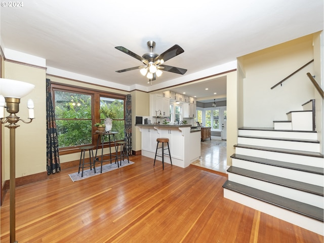 interior space featuring kitchen peninsula, a kitchen breakfast bar, ceiling fan, light hardwood / wood-style flooring, and white cabinetry