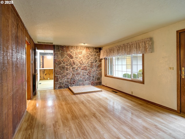 empty room with a textured ceiling, wood walls, and light hardwood / wood-style flooring