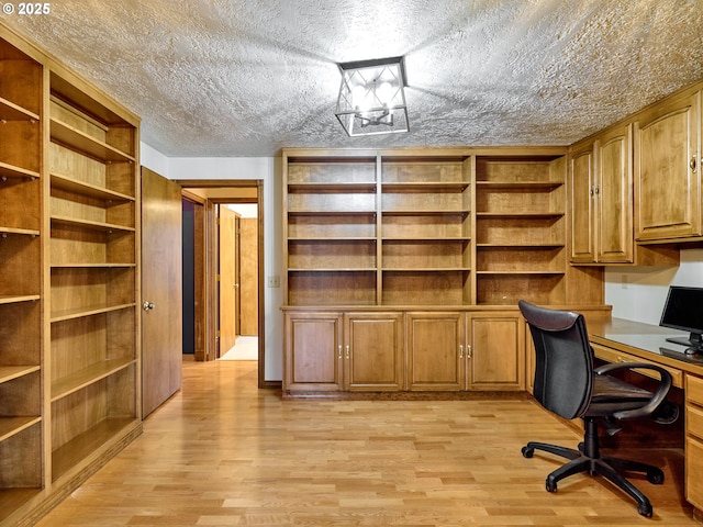 unfurnished office with built in desk, a textured ceiling, and light hardwood / wood-style flooring