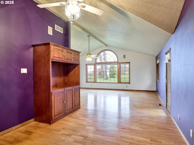 interior space featuring light wood-type flooring, ceiling fan, a textured ceiling, and vaulted ceiling with beams