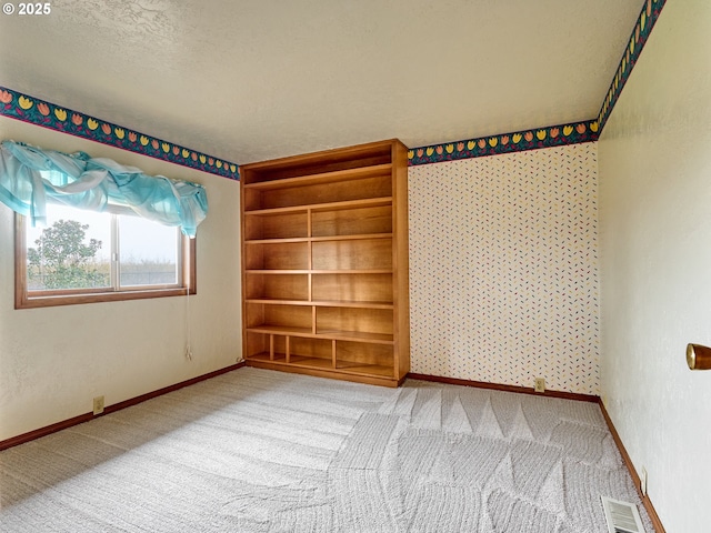 carpeted spare room with a textured ceiling and built in shelves