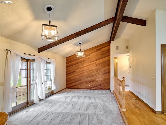 unfurnished living room with wooden walls, lofted ceiling with beams, and a chandelier