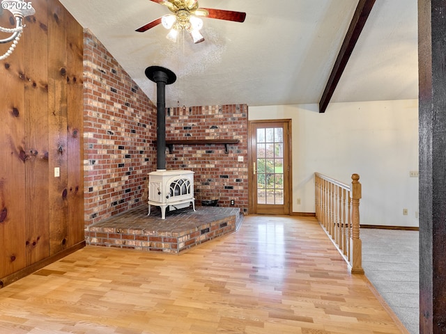 unfurnished living room with light hardwood / wood-style floors, vaulted ceiling with beams, a textured ceiling, and a wood stove