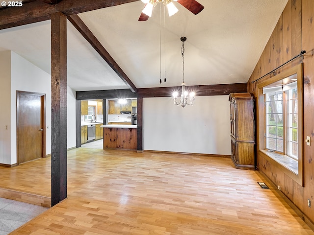 unfurnished dining area with sink, light hardwood / wood-style floors, wooden walls, ceiling fan with notable chandelier, and vaulted ceiling with beams