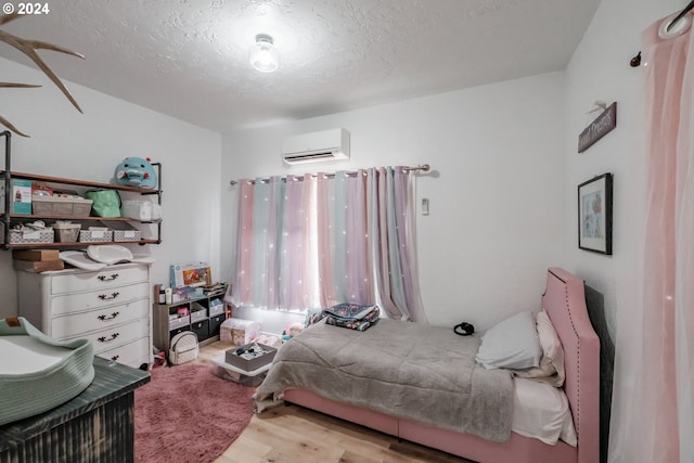 bedroom with a textured ceiling, wood finished floors, and a wall mounted AC