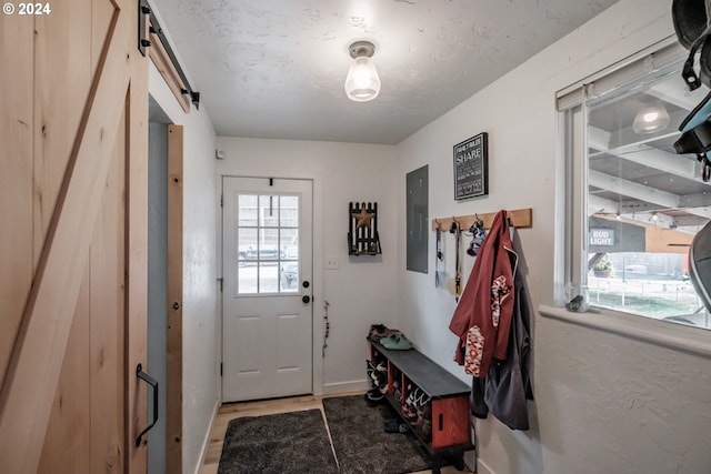 doorway with a textured ceiling, a barn door, wood finished floors, and electric panel