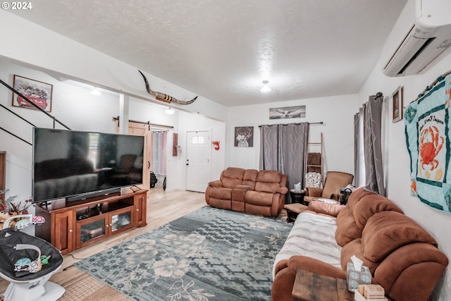 living room with a wall unit AC, light wood-type flooring, a barn door, and a textured ceiling