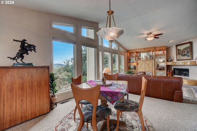 carpeted dining space featuring vaulted ceiling, a tiled fireplace, and ceiling fan