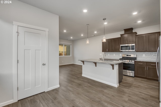 kitchen featuring a kitchen bar, an island with sink, appliances with stainless steel finishes, pendant lighting, and sink