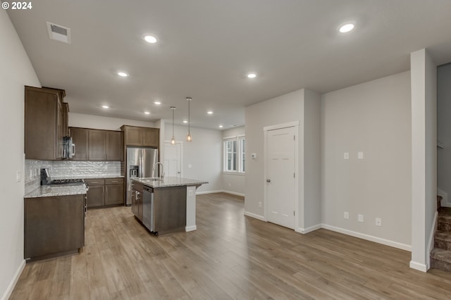 kitchen with decorative light fixtures, light hardwood / wood-style flooring, light stone counters, and a center island with sink