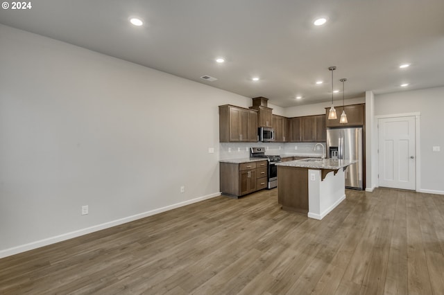 kitchen with hardwood / wood-style floors, a center island with sink, a breakfast bar area, stainless steel appliances, and backsplash