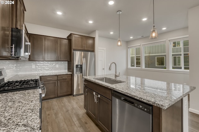 kitchen featuring an island with sink, stainless steel appliances, decorative backsplash, light stone counters, and sink