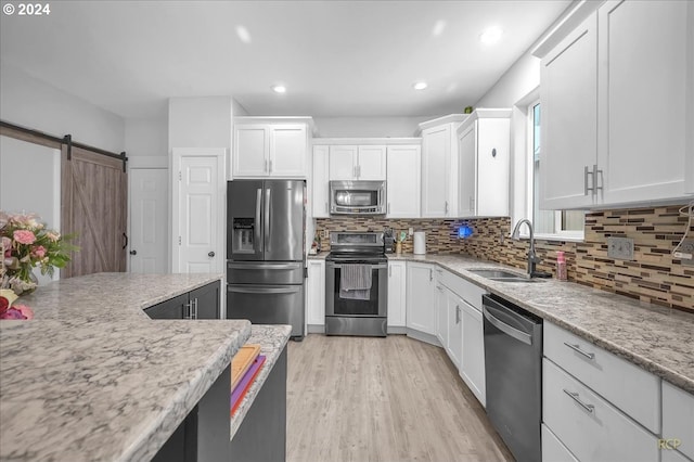 kitchen featuring white cabinets, appliances with stainless steel finishes, sink, light stone counters, and a barn door