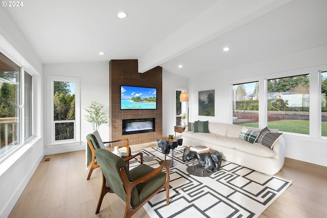 living room featuring a tiled fireplace, lofted ceiling with beams, and light hardwood / wood-style floors