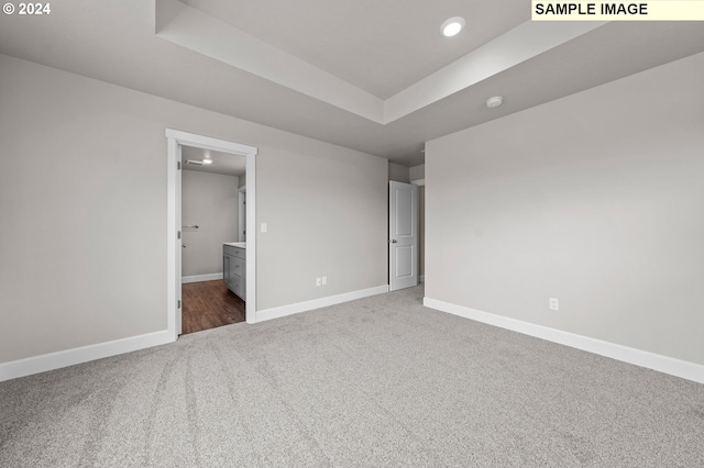 unfurnished bedroom featuring carpet, a raised ceiling, connected bathroom, and baseboards