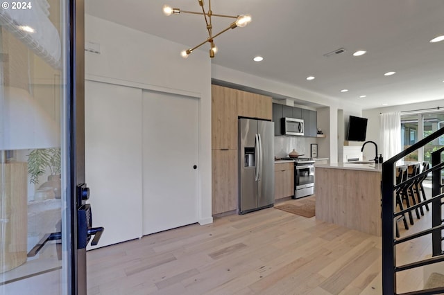 kitchen featuring light hardwood / wood-style floors, a center island with sink, tasteful backsplash, appliances with stainless steel finishes, and sink