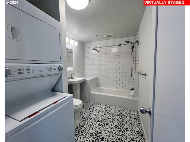 full bathroom featuring tiled shower / bath combo, tile flooring, toilet, stacked washer and clothes dryer, and sink