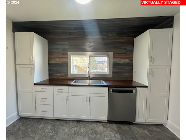 kitchen featuring wood walls, white cabinetry, dark tile flooring, dishwasher, and sink