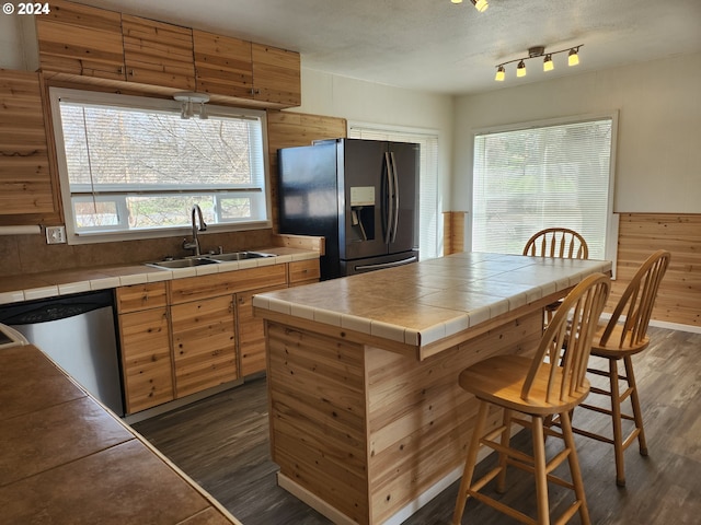 kitchen with black fridge, tile counters, dishwasher, sink, and a kitchen breakfast bar