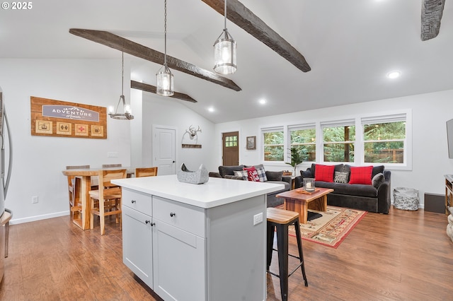 kitchen with vaulted ceiling with beams, light hardwood / wood-style floors, decorative light fixtures, a kitchen bar, and a kitchen island