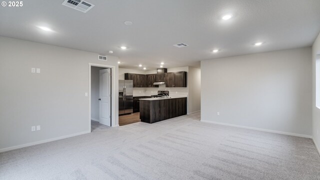 kitchen featuring light colored carpet, appliances with stainless steel finishes, a center island, and dark brown cabinets