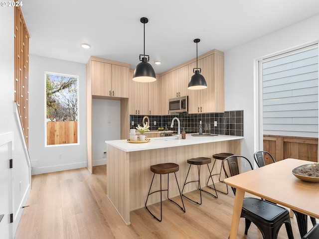 kitchen with kitchen peninsula, light brown cabinetry, backsplash, light hardwood / wood-style floors, and hanging light fixtures