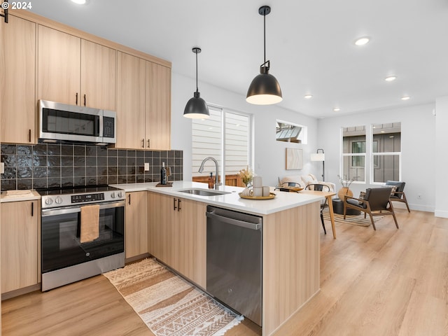 kitchen featuring light brown cabinets, sink, hanging light fixtures, light hardwood / wood-style flooring, and stainless steel appliances