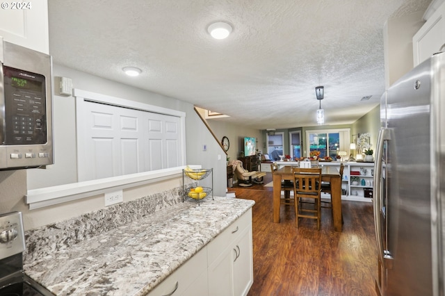 kitchen with a textured ceiling, stainless steel appliances, white cabinetry, and dark hardwood / wood-style floors