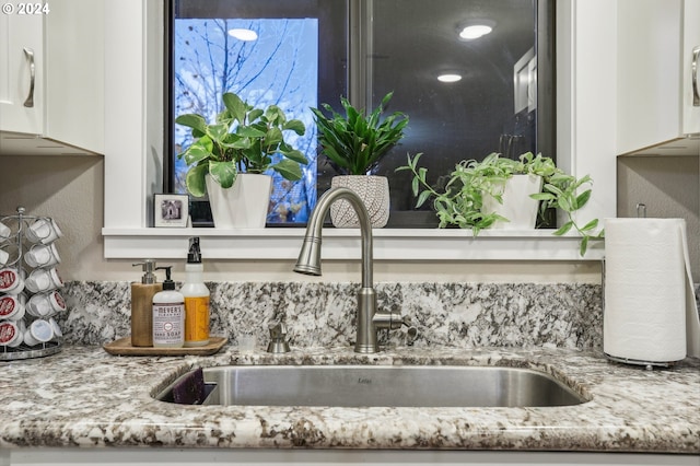 interior details featuring white cabinetry, sink, and light stone counters