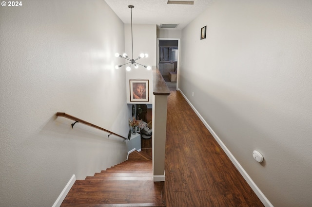 staircase featuring a chandelier, wood-type flooring, and a textured ceiling