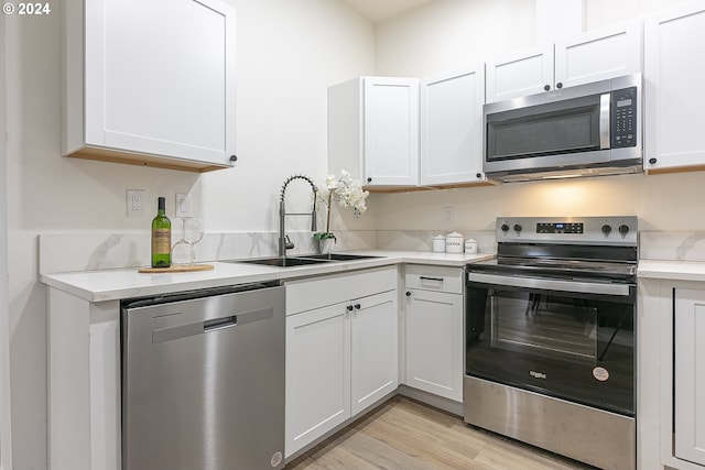 kitchen with white cabinets, sink, stainless steel appliances, and light hardwood / wood-style flooring