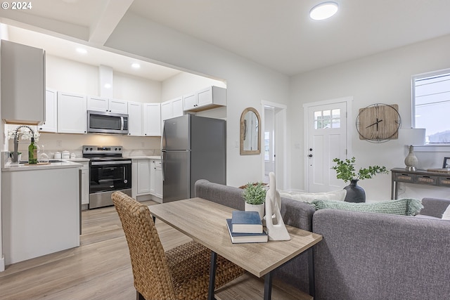 kitchen featuring beam ceiling, white cabinetry, sink, light hardwood / wood-style flooring, and appliances with stainless steel finishes