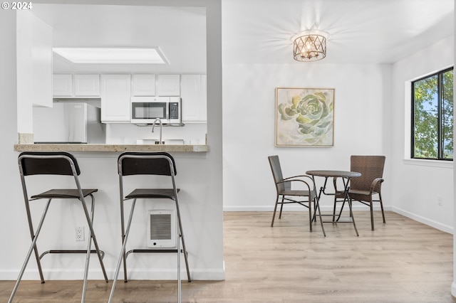 kitchen featuring refrigerator, sink, a notable chandelier, white cabinets, and light hardwood / wood-style floors