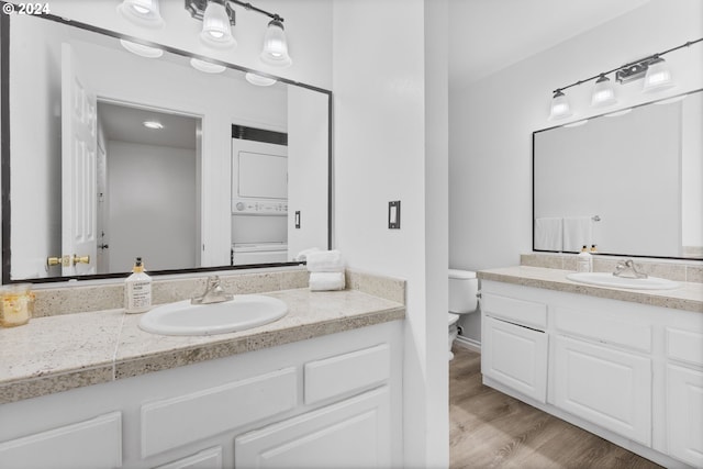 bathroom featuring hardwood / wood-style floors, vanity, toilet, and stacked washer and clothes dryer