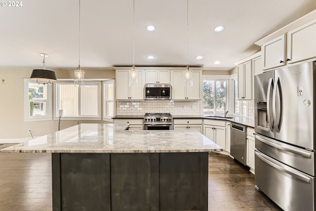 kitchen featuring light stone countertops, stainless steel appliances, sink, pendant lighting, and white cabinetry