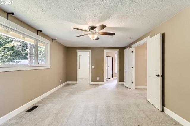 empty room featuring a textured ceiling, light colored carpet, and ceiling fan