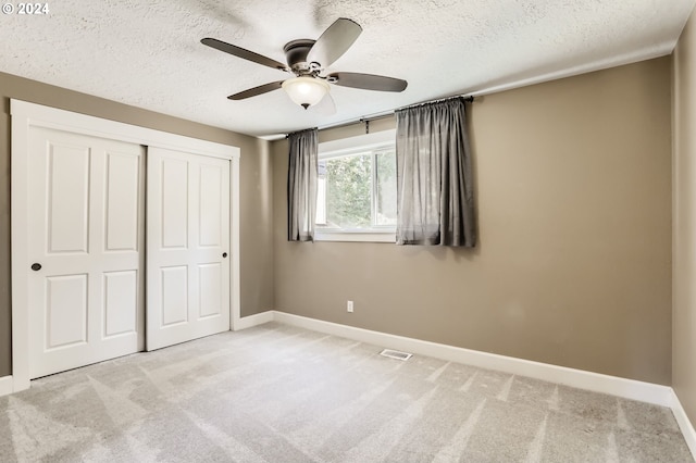 unfurnished bedroom featuring ceiling fan, light colored carpet, a textured ceiling, and a closet