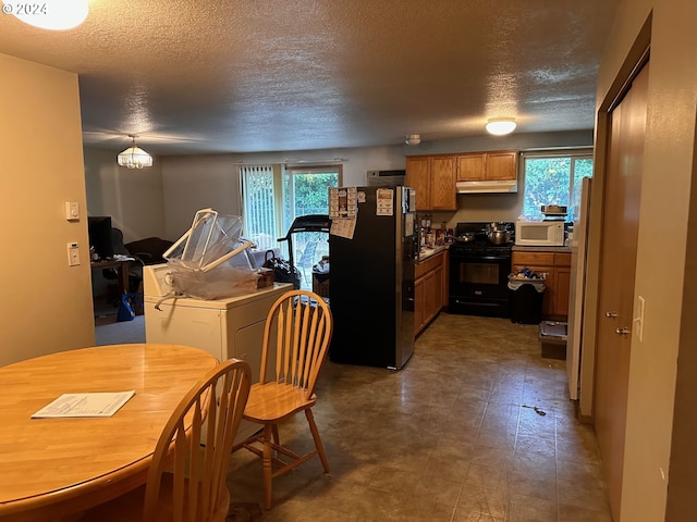 kitchen with a textured ceiling, freestanding refrigerator, white microwave, black gas range, and under cabinet range hood