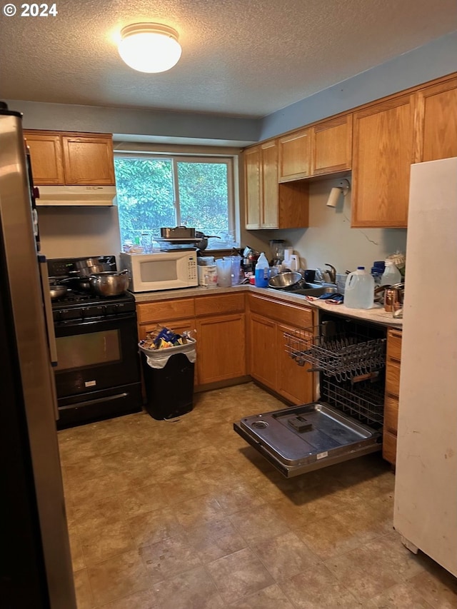 kitchen with a sink, a textured ceiling, under cabinet range hood, and white appliances