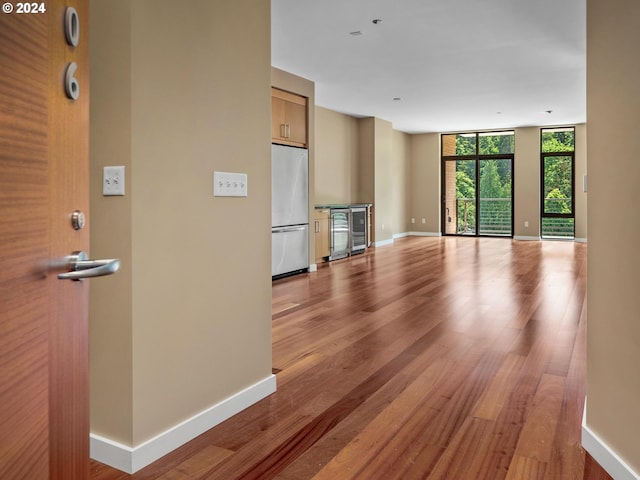 unfurnished living room featuring beverage cooler, light hardwood / wood-style floors, and floor to ceiling windows