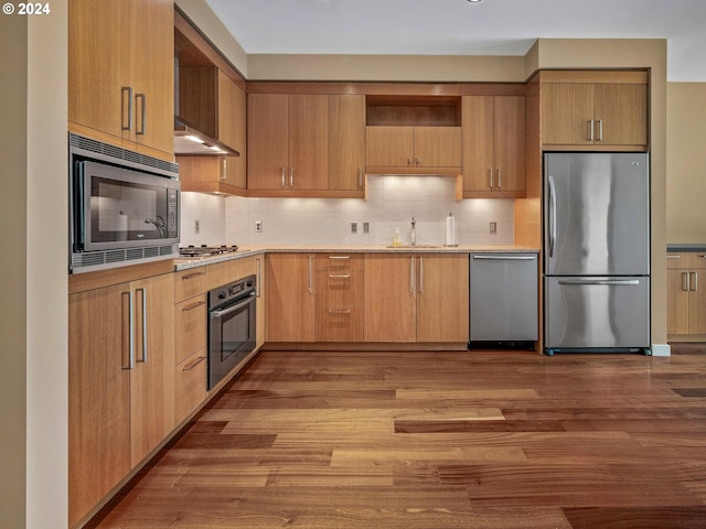 kitchen with sink, appliances with stainless steel finishes, light hardwood / wood-style floors, and tasteful backsplash