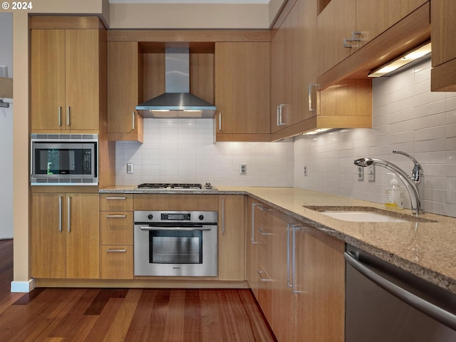 kitchen with wall chimney range hood, tasteful backsplash, appliances with stainless steel finishes, dark hardwood / wood-style floors, and sink