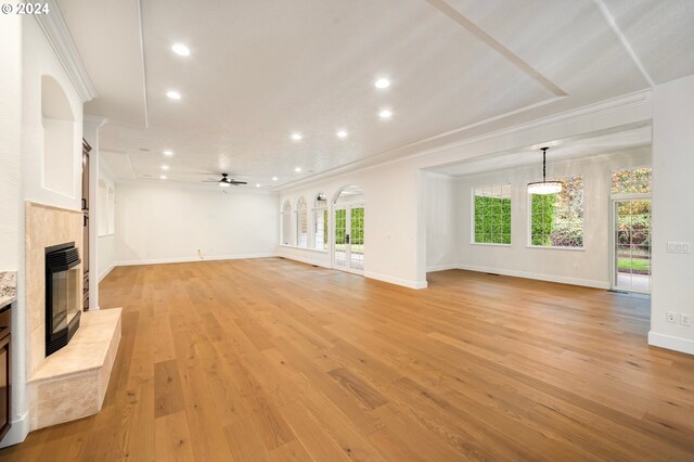 unfurnished living room with light wood-style flooring, a ceiling fan, a glass covered fireplace, crown molding, and baseboards