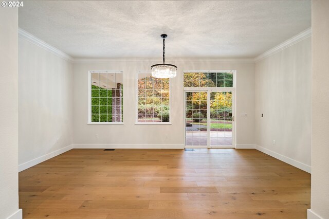 empty room featuring a textured ceiling, an inviting chandelier, crown molding, light wood finished floors, and baseboards