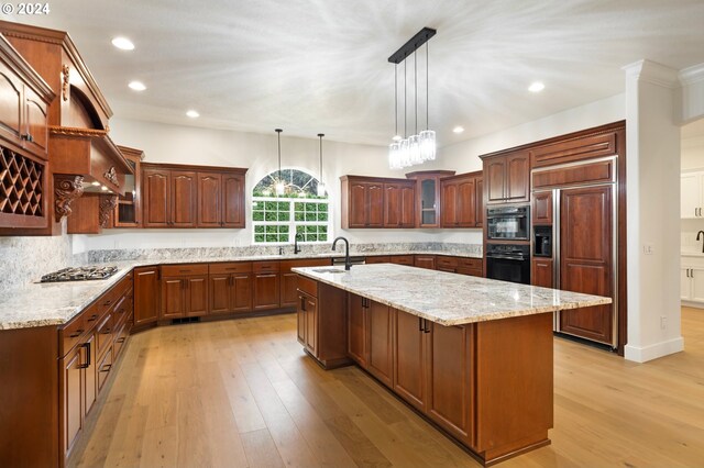 kitchen with a sink, light wood-style flooring, a kitchen island with sink, and paneled refrigerator