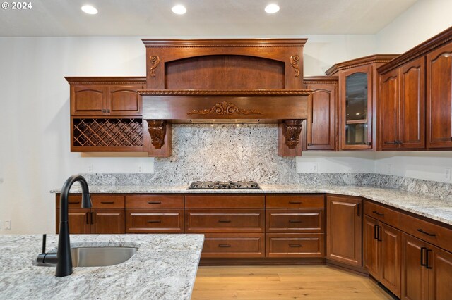 kitchen featuring glass insert cabinets, stainless steel gas cooktop, light stone counters, light wood-style flooring, and a sink