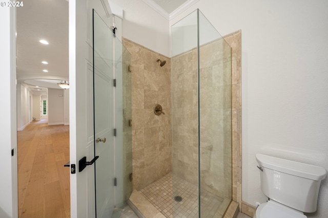 bathroom with wood finished floors, baseboards, ornamental molding, a shower stall, and toilet