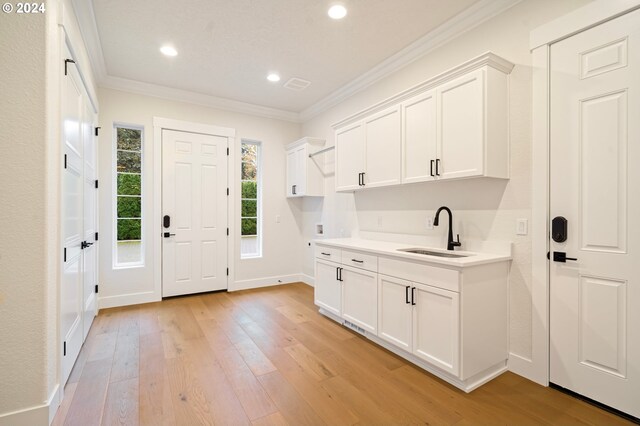 kitchen featuring crown molding, light countertops, light wood-style flooring, white cabinets, and a sink