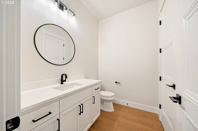 half bathroom with vanity, toilet, wood finished floors, and baseboards